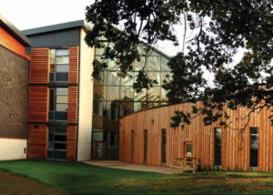 three storey timber clad large glazed building with a timber single storey curved extension