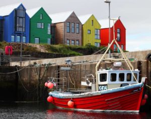 five multicolour timber buildings next to a harbour with a red boat berthed