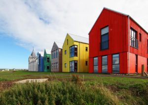 five multicolour timber buildings adjoined to an older building on a grassy area
