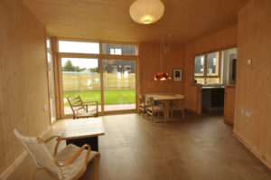 inside a timber room with timber furniture and a large double floor to ceiling window looking to a garden outside