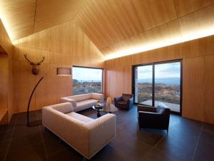 very modern timber interior room with modern furniture and up-lit ceiling looking out to hills and the sea