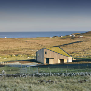 faceted timber building with a green living roof on an open landscape looking out to sea