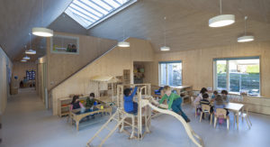 interior of a timber nursery room with play climbing frame with children on it and other children at tables learning