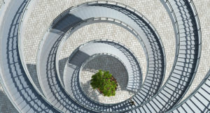 looking down a spiral staircase to a brick patterened floor with a tree in the middle