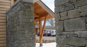 natural stone wall with a gap to walk through looking to a sloped timber roof structure overlooking a car park with parked cars