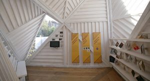 pyramid shaped timber interior of a pop up pavillion with exhibition text and books hanging from strings