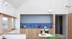 kitchen dining room with white painted timber walls, two tone blue kitchen infil on the wall and a window on the left looking out to the sea and hills