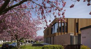two storey health centre with timber cladding on the upper floor, in a parkland setting with cherry blossom trees