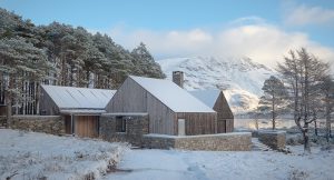 snow covered larch clad timber house surrounded by forest and a loch