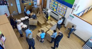 Adults observing children move boxes in a school space