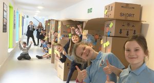 children with their thumbs up in a corridor filled with cardboard boxes