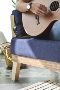 man with guitar sitting on a blue cushioned sofa