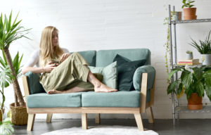 woman sitting ona. sofa with a white wall background and plant on shelving
