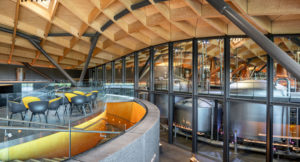 seating o a first floor bar with complex waffle timber roof looking into huge whiskey stills behind a glazed wall